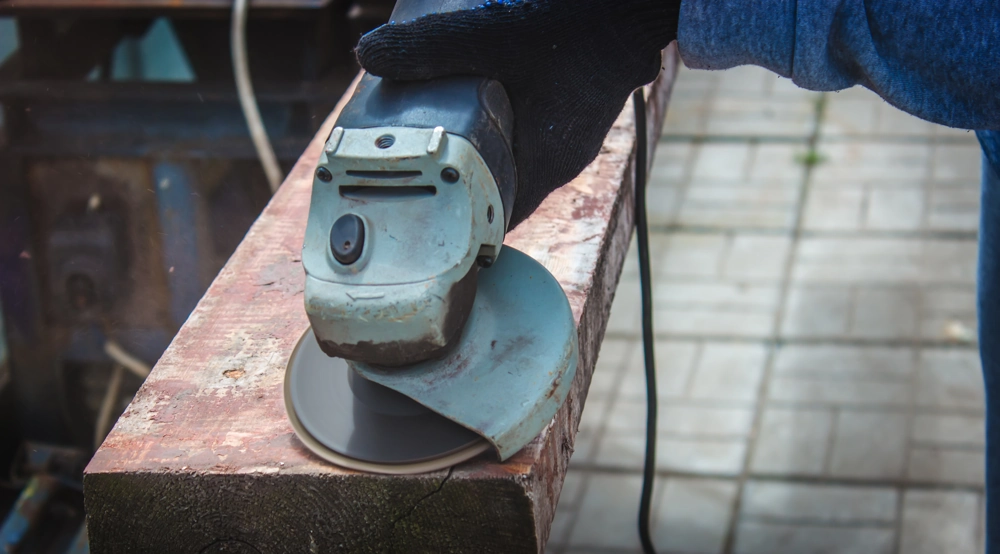 Ręczna szlifierka kątowa z tarczą ścierną wygładza powierzchnię metalowej belki