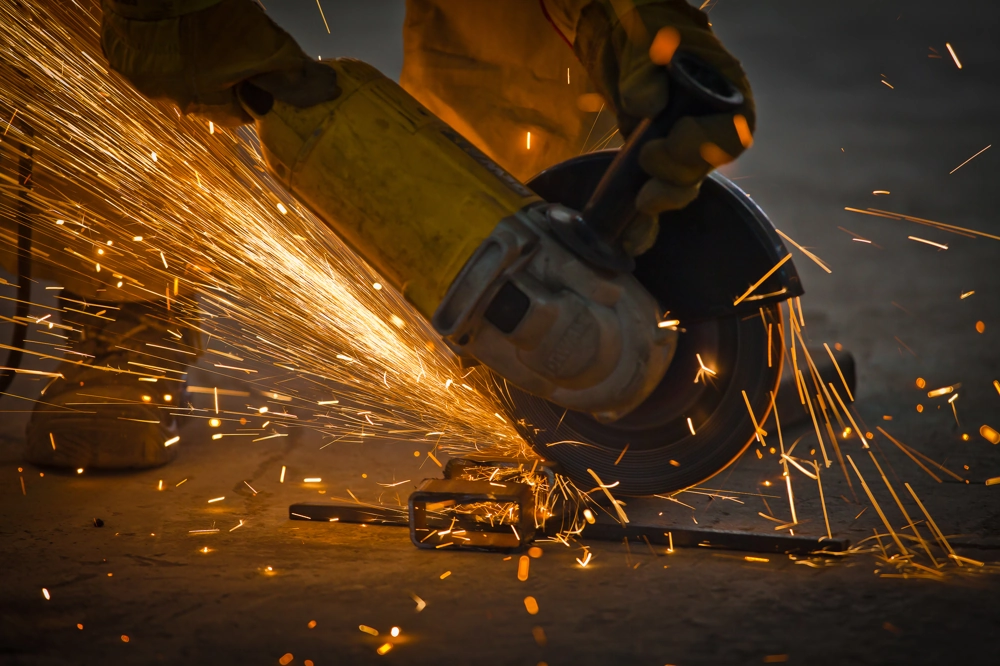 Szlifowanie metalowego elementu na posadzce za pomocą szlifierki kątowej, widoczne iskry