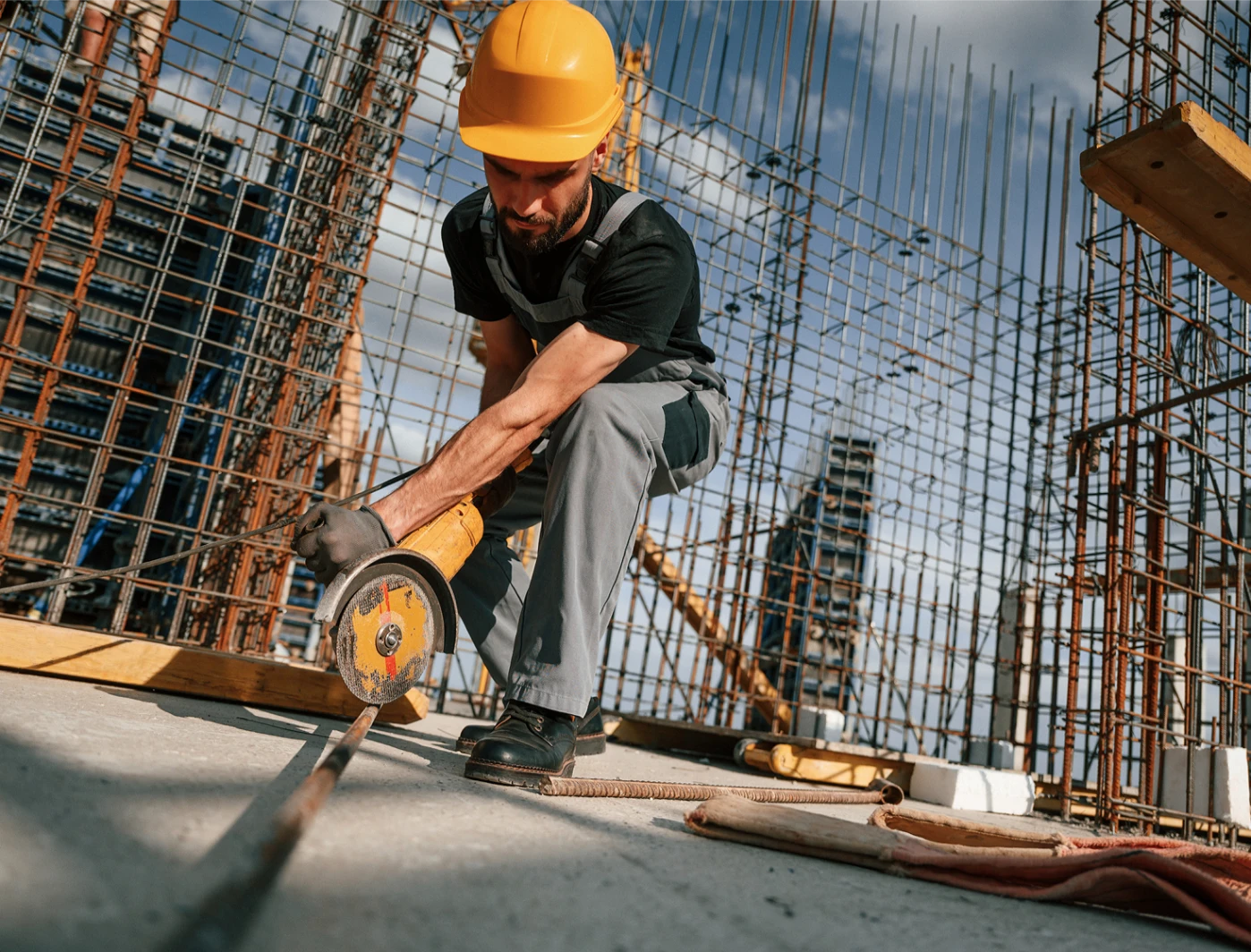 Robotnik w kasku tnie pręt zbrojeniowy tarczą szlifierską na placu budowy
