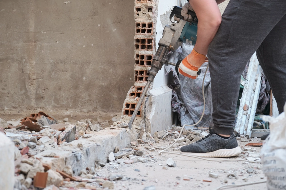 Operator rozbija beton młotem wyburzeniowym w ścianie, kucie betonu